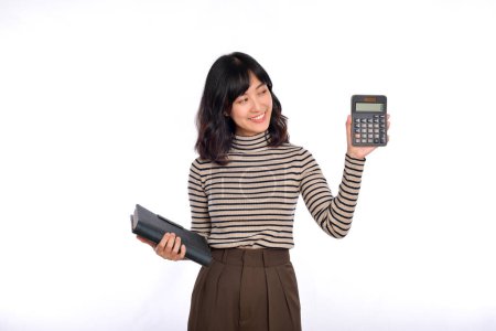 Foto de Young Asian woman casual uniform holding white piggy bank and notebook isolated on white background. Financial and bank saving money concept - Imagen libre de derechos