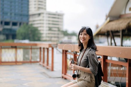 Téléchargez les photos : Young Asian woman backpack traveler using mobile phone in express boat pier on Chao Phraya River in Bangkok. Journey trip lifestyle, world travel explorer. - en image libre de droit