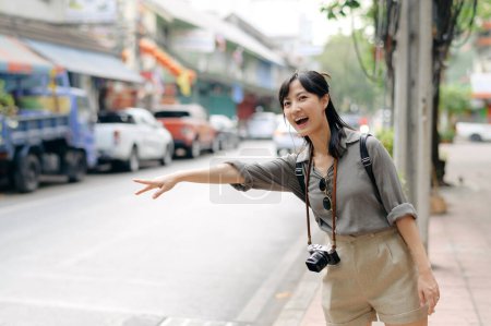 Téléchargez les photos : Smiling young Asian woman traveler hitchhiking on a road in the city. - en image libre de droit