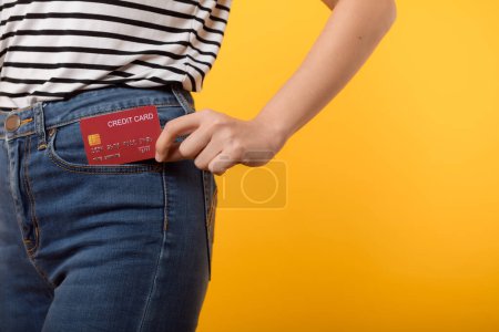 Photo for Hand of person woman holding plastic credit card out of the pocket blue jean plants isolated on yellow studio background. online shopping payment, currency, bill, pay money, finance concept. - Royalty Free Image