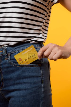 Photo for Hand of person woman holding plastic credit card out of the pocket blue jean plants isolated on yellow studio background. online shopping payment, currency, bill, pay money, finance concept. - Royalty Free Image