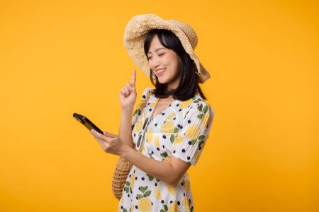 Téléchargez les photos : Portrait heureuse jeune femme asiatique avec la mode robe de printemps en utilisant l'application mobile pour la publicité isolée sur fond jaune. Concept de technologie d'application Smartphone. - en image libre de droit