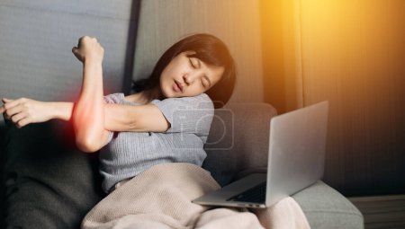 Foto de Asian woman has shoulder pain while working on laptop at home. People with body-muscles problem. - Imagen libre de derechos