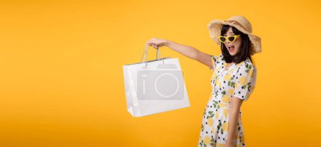 Photo for Portrait attractive happy young asian woman with trendy springtime dress, hat, sunglasses fashion and paper bag isolated on yellow background. Summertime sale shopping concept. - Royalty Free Image