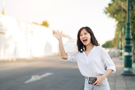 Foto de Retrato joven hermosa mujer asiática saludando de la mano a un amigo por la calle en unas vacaciones soleadas. - Imagen libre de derechos