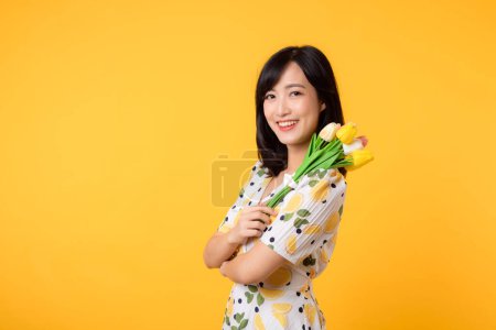 Téléchargez les photos : Studio portrait jolie jeune femme asiatique heureux sourire habillage printemps mode tenant bouquet de tulipes fleur sur fond de studio jaune. Concept de vacances pour personne. - en image libre de droit