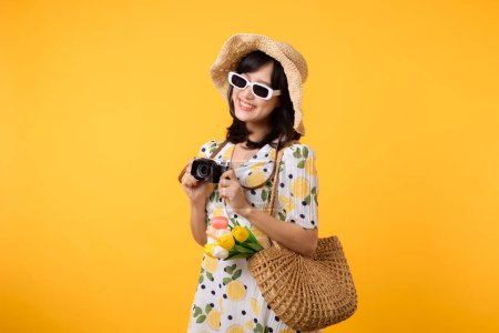 Photo for Studio portrait pretty young asian woman happy smile dressing springtime fashion with sunglasses, woven bag and holding tulip bouquet flower and camera against yellow studio background. Travel concept - Royalty Free Image