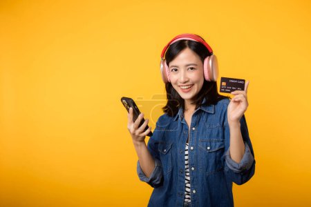 Photo for Portrait asian young woman with happy success smile wearing denim clothes and headphone holding smartphone and credit card. Shopping online mobile phone entertainment lifestyle concept. - Royalty Free Image