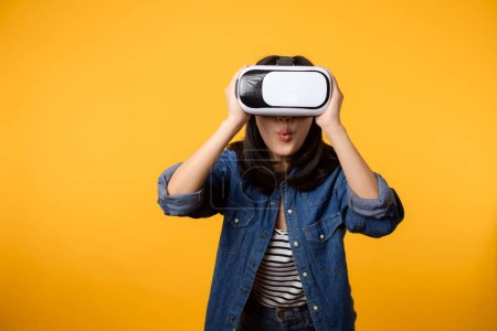 Photo for Asian young woman happy success wearing virtual reality headset game entertainment isolated on yellow background. Winner of cyber future video game concept. - Royalty Free Image