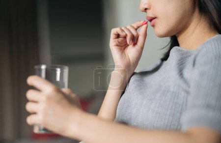 Téléchargez les photos : Closeup on medicine pill in hand of ill young woman laying on a sofa - en image libre de droit