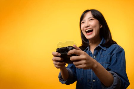 Photo for Portrait asian young woman with happy success smile wearing denim clothes holding joystick controller and playing video game. Fun and relax hobby entertainment lifestyle concept. - Royalty Free Image