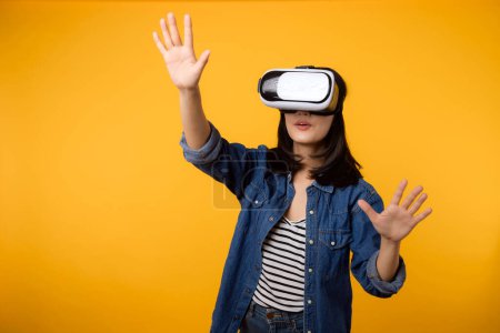 Foto de Asiático joven mujer feliz éxito usando realidad virtual juego de auriculares entretenimiento aislado sobre fondo amarillo. Ganador del concepto de videojuego de futuro cibernético. - Imagen libre de derechos