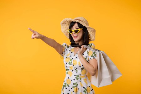 Photo for Portrait attractive happy young asian woman with trendy springtime dress, hat, sunglasses fashion and paper bag isolated on yellow background. Summertime sale shopping concept. - Royalty Free Image