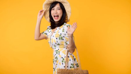 Téléchargez les photos : Portrait attrayant jeune femme asiatique heureuse avec robe de printemps à la mode, chapeau, lunettes de soleil mode et sac tissé isolé sur fond jaune. Vente d'été concept de shopping. - en image libre de droit