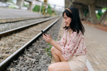 Foto de Joven mujer asiática viajero con cesta de tejido utilizando un teléfono móvil al lado de la estación de tren en Bangkok. Viaje viaje estilo de vida, viajero mundial o concepto de turismo de verano de Asia. - Imagen libre de derechos