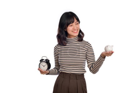 Photo for Happy Asian woman with sweater shirt holding alarm clock and piggy bank on white background. - Royalty Free Image