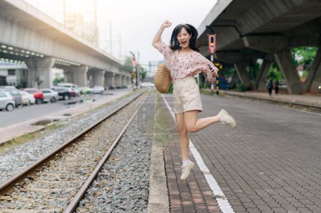 Téléchargez les photos : Jeune voyageuse asiatique sautant à côté de la gare ferroviaire de Bangkok. Voyage voyage style de vie, monde Voyage explorer ou Asie concept de tourisme d'été. - en image libre de droit