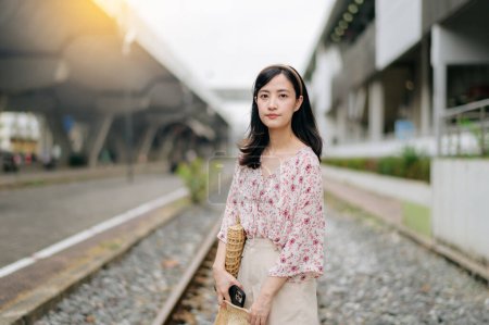 Téléchargez les photos : Asiatique jeune femme voyageur avec panier à tisser heureux souriant regardant à une caméra à côté de train ferroviaire. Voyage voyage style de vie, monde Voyage explorer ou Asie concept de tourisme d'été. - en image libre de droit