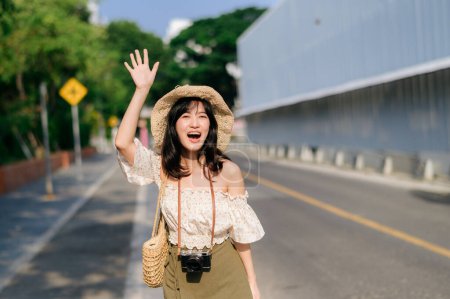 Foto de Retrato de una joven mujer asiática viajera con sombrero de tejer y canasta y una cámara saludando de la mano a un amigo por la calle. Viaje viaje estilo de vida, viajero mundial o concepto de turismo de verano de Asia. - Imagen libre de derechos