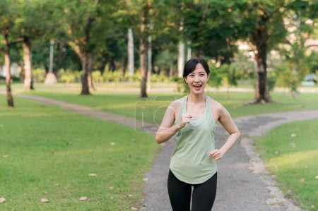 Téléchargez les photos : Fit asiatique jeune femme jogging dans le parc souriant course heureuse et profiter d'un mode de vie sain en plein air. Joggeuse. Fitness fille coureuse dans le parc public. mode de vie sain et concept de bien-être - en image libre de droit