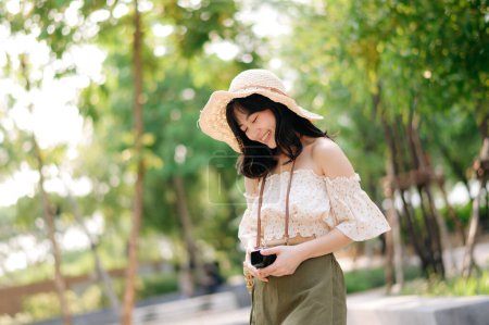 Photo for Portrait of young asian woman traveler with weaving hat and basket and a camera on green public park nature background. Journey trip lifestyle, world travel explorer or Asia summer tourism concept. - Royalty Free Image