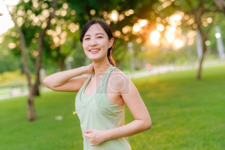 Foto de Una corredora. Ajuste mujer joven asiática con ropa deportiva verde estiramiento muscular en el parque antes de correr y disfrutar de un sano al aire libre. Chica corredor de fitness en el parque público. Bienestar siendo concepto - Imagen libre de derechos