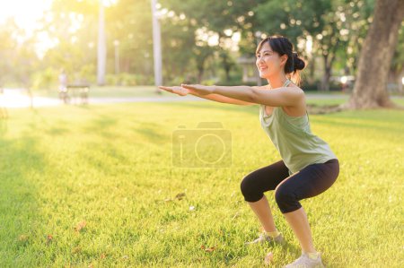Foto de Una corredora. Ajuste mujer joven asiática con ropa deportiva verde en cuclillas en el parque antes de correr y disfrutar de un aire libre saludable. Chica corredor de fitness en el parque público. Bienestar siendo concepto - Imagen libre de derechos
