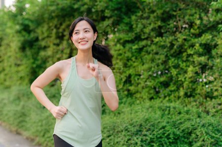 Téléchargez les photos : S'adapter jeune femme asiatique jogging dans le parc souriant course heureuse et profiter d'un mode de vie sain en plein air. Joggeuse. Fitness fille coureuse dans le parc public. mode de vie sain et concept de bien-être - en image libre de droit