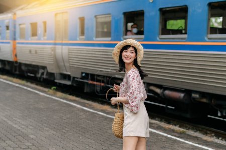 Photo for Asian young woman traveler with weaving basket looking back happy smiling to a camera beside train coming background. Journey trip lifestyle, world travel explorer or Asia summer tourism concept. - Royalty Free Image