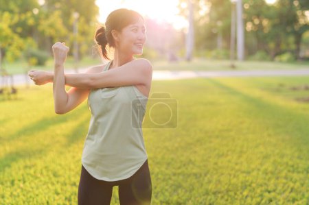 Téléchargez les photos : Joggeuse. Adaptez la jeune femme asiatique avec le muscle vert d'étirement de vêtements de sport dans le parc avant de courir et de profiter d'un plein air sain. Fitness fille coureuse dans le parc public. Concept de bien-être - en image libre de droit