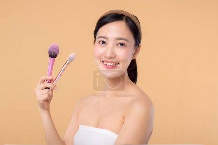 Photo for Portrait young happy asian woman with natural make up face holding cosmetic skin powder blusher isolated on beige background. Female apply skincare brush treatment. beauty product, cosmetology concept. - Royalty Free Image