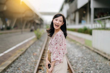 Téléchargez les photos : Asiatique jeune femme voyageur avec panier à tisser heureux souriant regardant à une caméra à côté de train ferroviaire. Voyage voyage style de vie, monde Voyage explorer ou Asie concept de tourisme d'été. - en image libre de droit