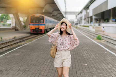 Photo for Asian young woman traveler with weaving basket happy smiling and looking to a camera beside train coming background. Journey trip lifestyle, world travel explorer or Asia summer tourism concept. - Royalty Free Image