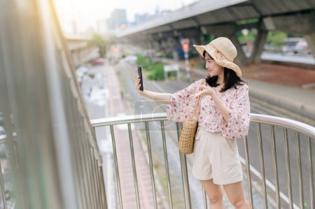 Photo for Asian young woman traveler with weaving basket using mobile phone and standing on overpass with railway background. Journey trip lifestyle, world travel explorer or Asia summer tourism concept. - Royalty Free Image