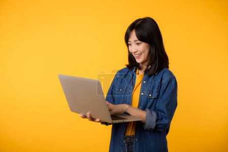 Photo for Portrait happy young woman wearing yellow t-shirt and denim shirt holding laptop and use notebook isolated on yellow studio background. business technology application communication concept. - Royalty Free Image
