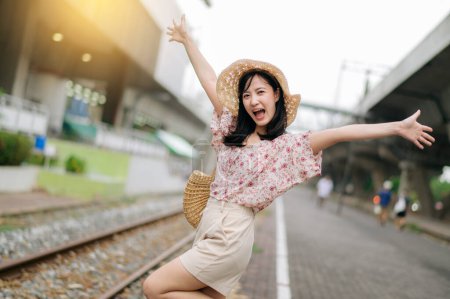 Photo for Asian young woman traveler with weaving basket happy smiling looking to a camera beside train railway. Journey trip lifestyle, world travel explorer or Asia summer tourism concept. - Royalty Free Image