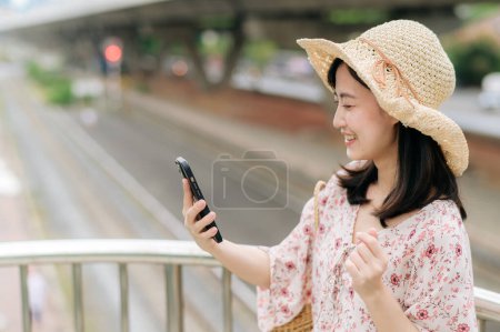 Foto de Asiático joven viajero con tejer cesta usando teléfono móvil y de pie en puente con fondo de ferrocarril. Viaje viaje estilo de vida, viajero mundial o concepto de turismo de verano de Asia. - Imagen libre de derechos