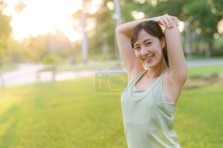 Téléchargez les photos : Joggeuse. Adaptez la jeune femme asiatique avec le muscle vert d'étirement de vêtements de sport dans le parc avant de courir et de profiter d'un plein air sain. Fitness fille coureuse dans le parc public. Concept de bien-être - en image libre de droit