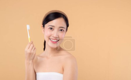 Téléchargez les photos : Portrait jeune femme de beauté avec un sourire heureux et sain tenant la brosse à dents dans sa main le matin isolé sur fond de studio beige. hygiène dent bouche soins propres et concept dentaire. - en image libre de droit
