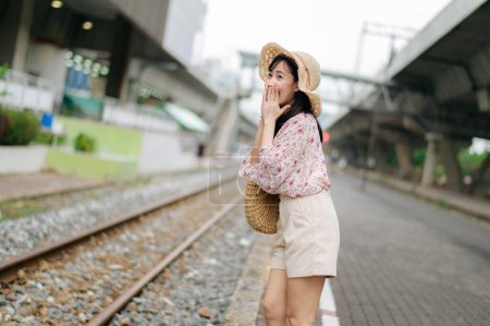 Foto de Asiático joven viajero con tejer cesta feliz sonriendo mirando a una cámara junto tren ferrocarril. Viaje viaje estilo de vida, viajero mundial o concepto de turismo de verano de Asia. - Imagen libre de derechos