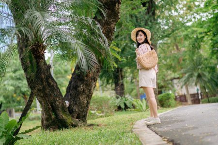 Photo for Portrait of young asian woman traveler with weaving hat and basket happy smile on green public park nature background. Journey trip lifestyle, world travel explorer or Asia summer tourism concept. - Royalty Free Image