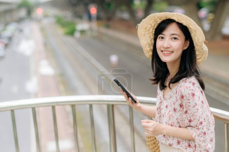 Photo for Asian young woman traveler with weaving basket using mobile phone and standing on overpass with railway background. Journey trip lifestyle, world travel explorer or Asia summer tourism concept. - Royalty Free Image