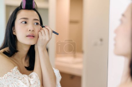 Photo for Beautiful Asian young woman applying makeup in front of the mirror. Lifestyle people concept. Advertisement for skin cream, anti-wrinkle cream, baby face - Royalty Free Image
