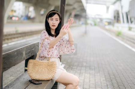 Foto de Joven mujer asiática viajero mirando su cara en un espejo y esperando tren en la estación de tren. Viaje viaje estilo de vida, viajero mundial o concepto de turismo de verano de Asia. - Imagen libre de derechos