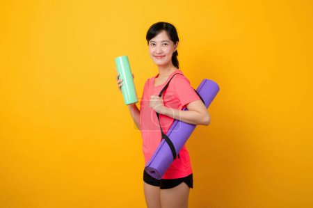Photo for Portrait asian young sports fitness woman happy smile wearing pink sportswear and yoga mat doing exercise training workout against yellow studio background. Healthy wellness lifestyle concept. - Royalty Free Image