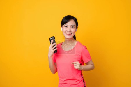 Photo for Portrait asian young sports fitness woman happy smile wearing pink sportswear and smartphone doing exercise training workout against yellow studio background. technology wellness lifestyle concept. - Royalty Free Image