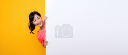 Foto de Asiático joven deportes fitness mujer feliz sonrisa usando rosa ropa deportiva de pie detrás de la bandera blanca en blanco o espacio vacío tablero de anuncios sobre fondo amarillo. bienestar concepto de estilo de vida. - Imagen libre de derechos