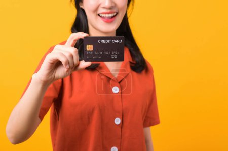 Téléchargez les photos : Portrait belle jeune femme asiatique sourire heureux habillé de vêtements orange montrant carte de crédit isolé sur fond jaune. Paiement et achat shopping concept de paiement. - en image libre de droit