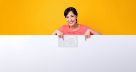 Téléchargez les photos : Asiatique jeune sport fitness femme heureux sourire portant des vêtements de sport rose debout derrière la bannière blanche vierge ou vide espace panneau publicitaire sur fond jaune. bien-être concept de style de vie. - en image libre de droit
