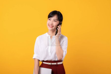 Foto de Retrato joven hermosa mujer asiática emprendedor feliz sonrisa usando camisa blanca y plantas rojas usando teléfono inteligente y la celebración de aislamiento portátil sobre fondo amarillo. - Imagen libre de derechos